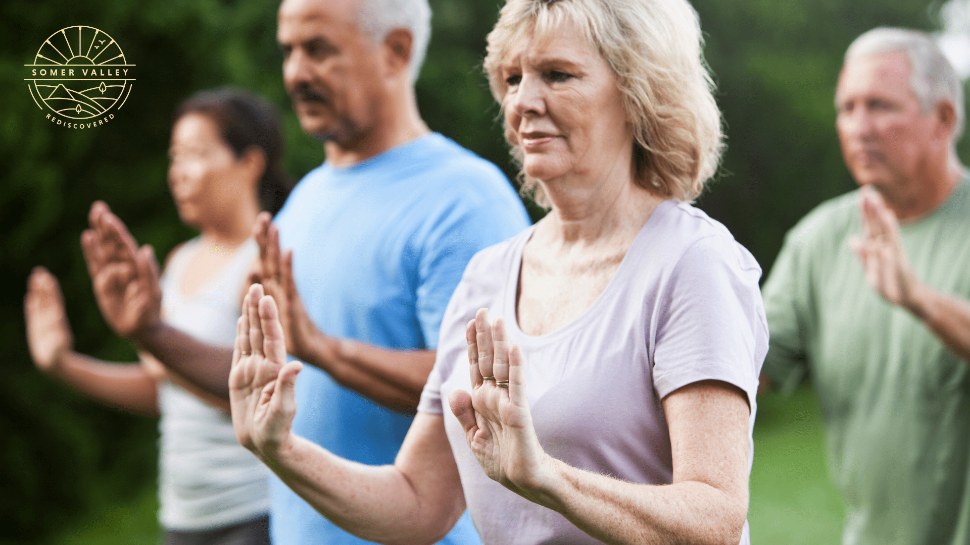 Two man and two women are taking part in a tai chi class. They have their arms at right angles and are pushing their palms away from their bodies.